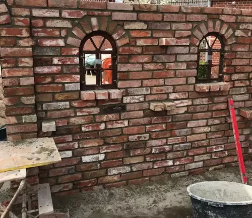 Rustikale Gartenmauer mit Rundbogen-Fenstern während der Bauphase.